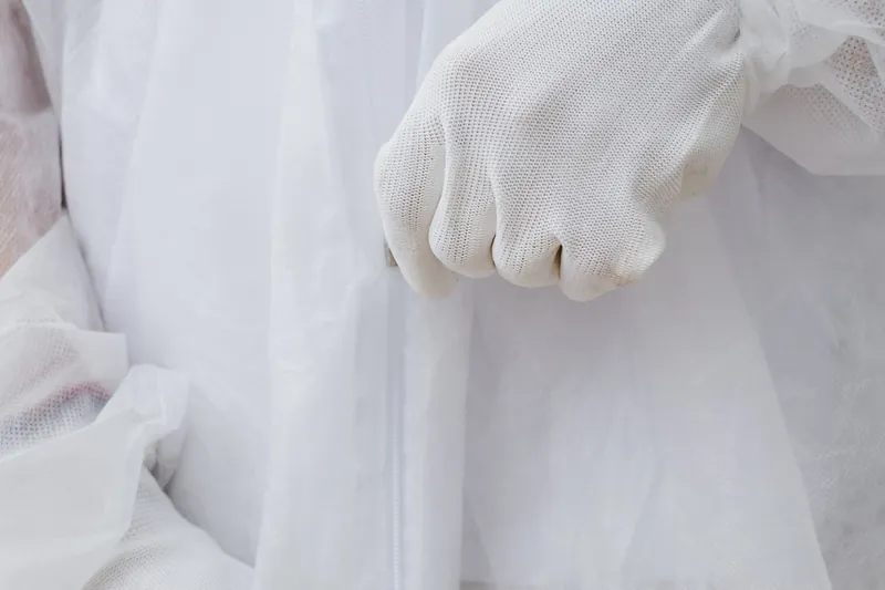 Gloved hands folded in front of a white disposable protective suit